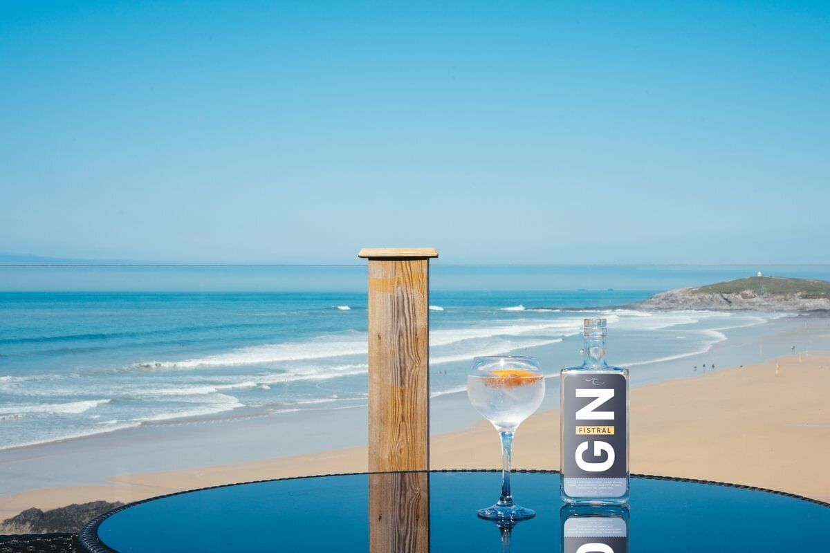 Un tavolo con una bottiglia di gin e un bicchiere su una spiaggia che si affaccia sull'oceano.