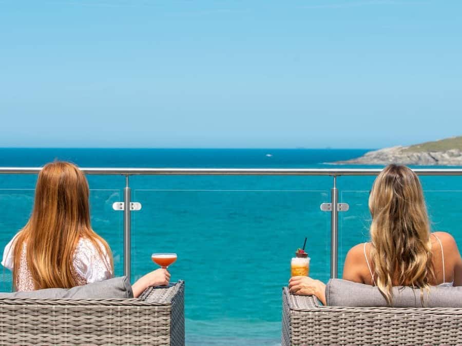 Two wicker lounge chairs facing a body of water with a clear sky and a distant landmass.