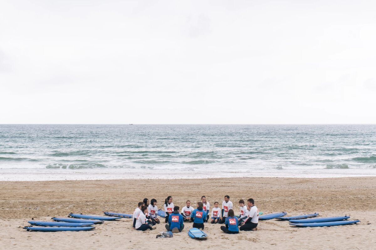 A group of people sitting on a beach with surfboards, facing the ocean.