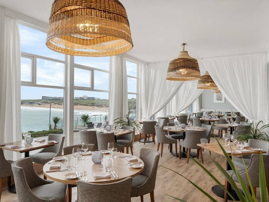 A restaurant with round tables, white curtains, and wicker pendant lights.