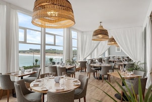 Un restaurante con mesas redondas, cortinas blancas y lámparas colgantes de mimbre.