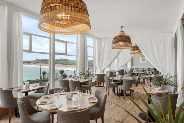 Un restaurante con mesas redondas, cortinas blancas y lámparas colgantes de mimbre.