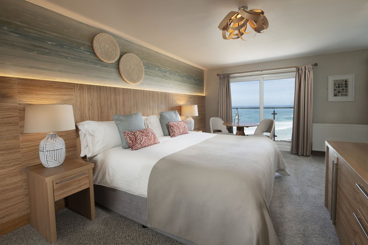 Een hotelkamer met een groot bed, een bureau en uitzicht op de oceaan.