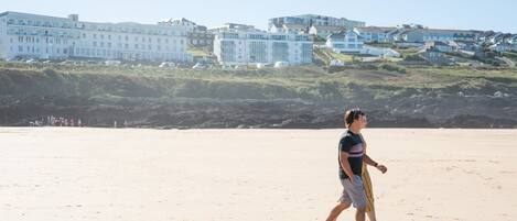 Ein Sandstrand mit einer Person, die entlanggeht, Gebäuden im Hintergrund und einem klaren Himmel.
