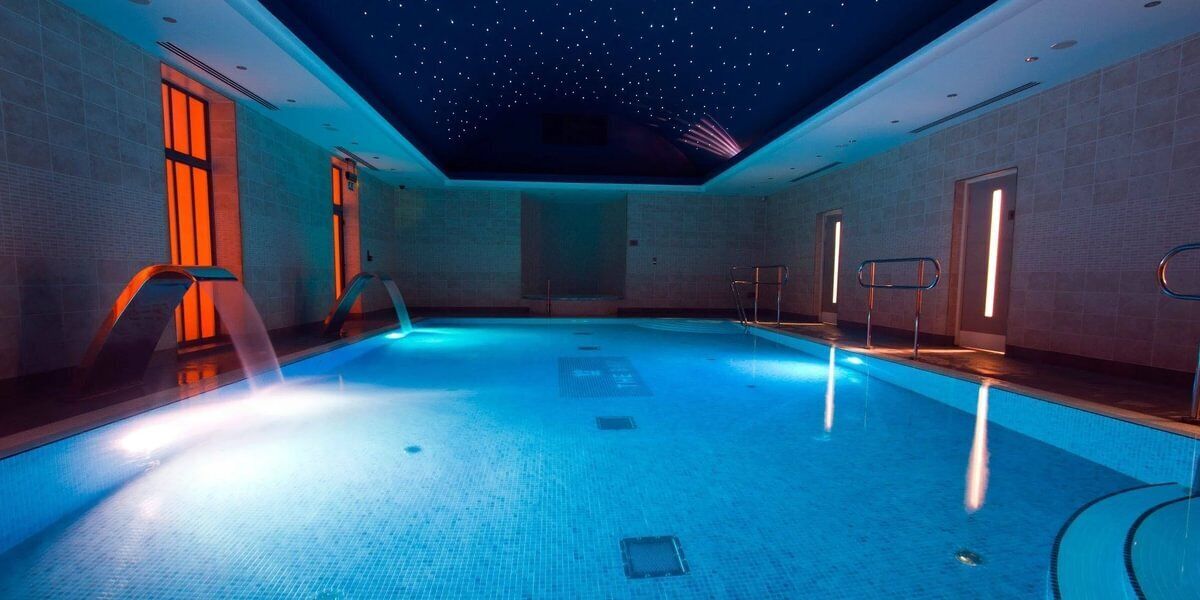 A swimming pool with a starry ceiling, surrounded by walls with doors and railings.