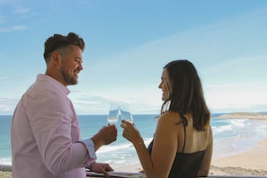 Een stel dat met wijn glazen proost op een locatie aan het strand, met uitzicht op de oceaan.