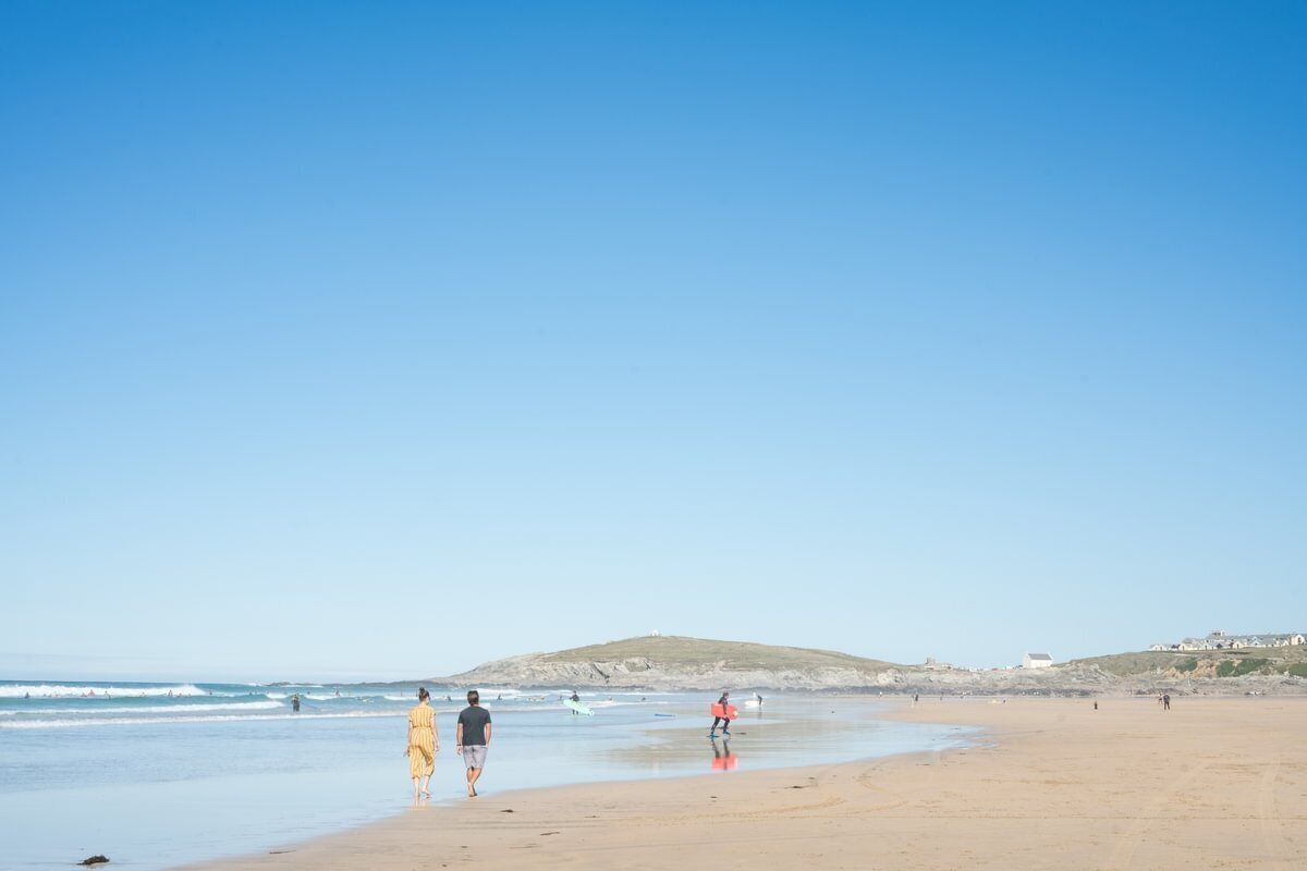 A beach with people walking, a sandy shore, and a hill in the background.