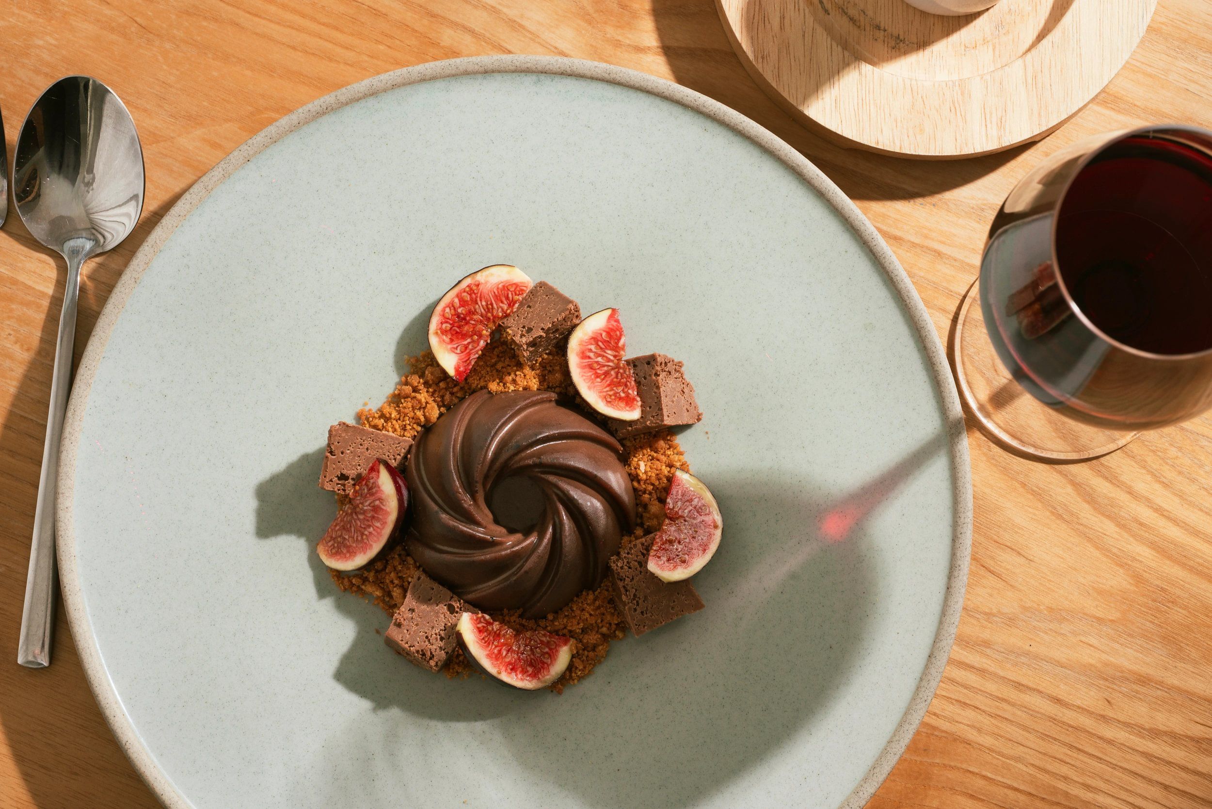 A dessert on a plate with a spoon and a glass of red liquid beside it.