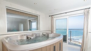 Une salle de bain moderne avec un jacuzzi, un grand miroir et une vue sur l’océan.