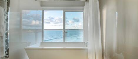 Un baño moderno con bañera, cabina de ducha de vidrio y un amplio ventanal con vistas al mar.