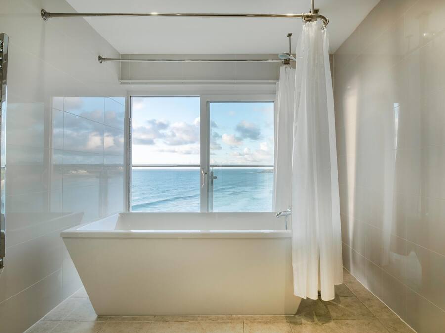 Une salle de bain moderne dotée d’une baignoire, d’une douche à parois de verre et d’une grande fenêtre offrant une vue sur la mer.