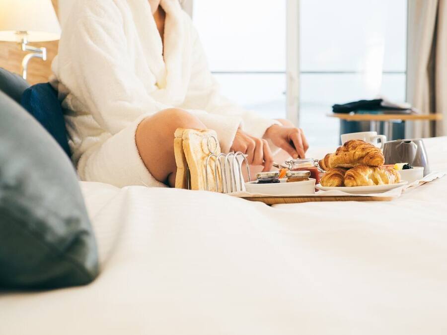 Una persona sentada en una cama con artículos de desayuno, como cruasanes, una taza y un plato.