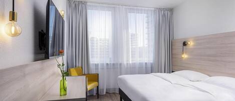 Una habitación de hotel con cama, escritorio, silla, televisión y ventana con cortinas.