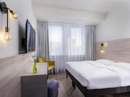 Ein Hotelzimmer mit Bett, Schreibtisch, Stuhl, Fernseher und einem Fenster mit Vorhängen.