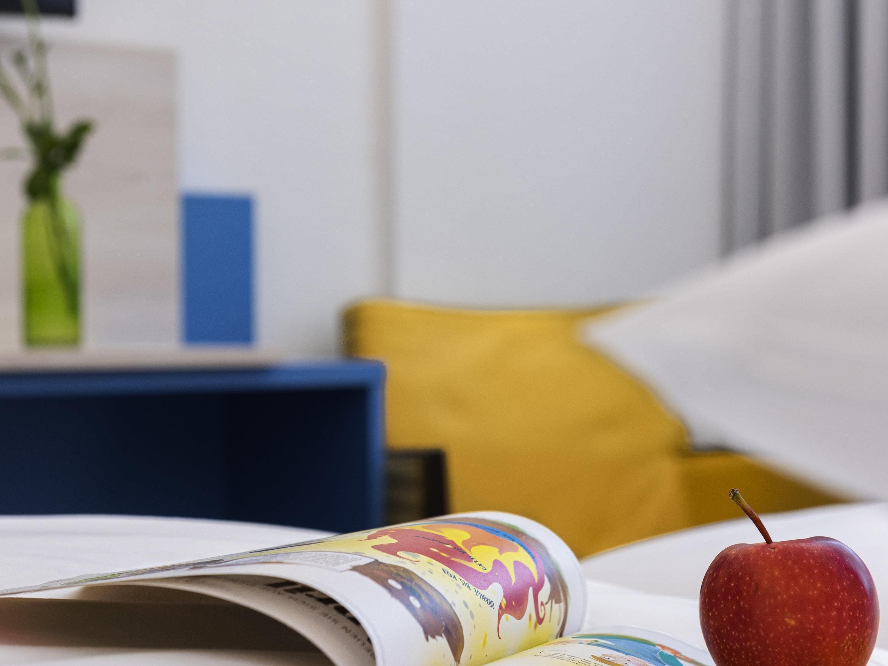A magazine with a colorful cover, a red apple, a blue chair, and a yellow pillow in a room.