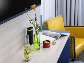 Una mesa con una botella, un florero verde con una flor, un vaso negro, una taza roja y una revista.