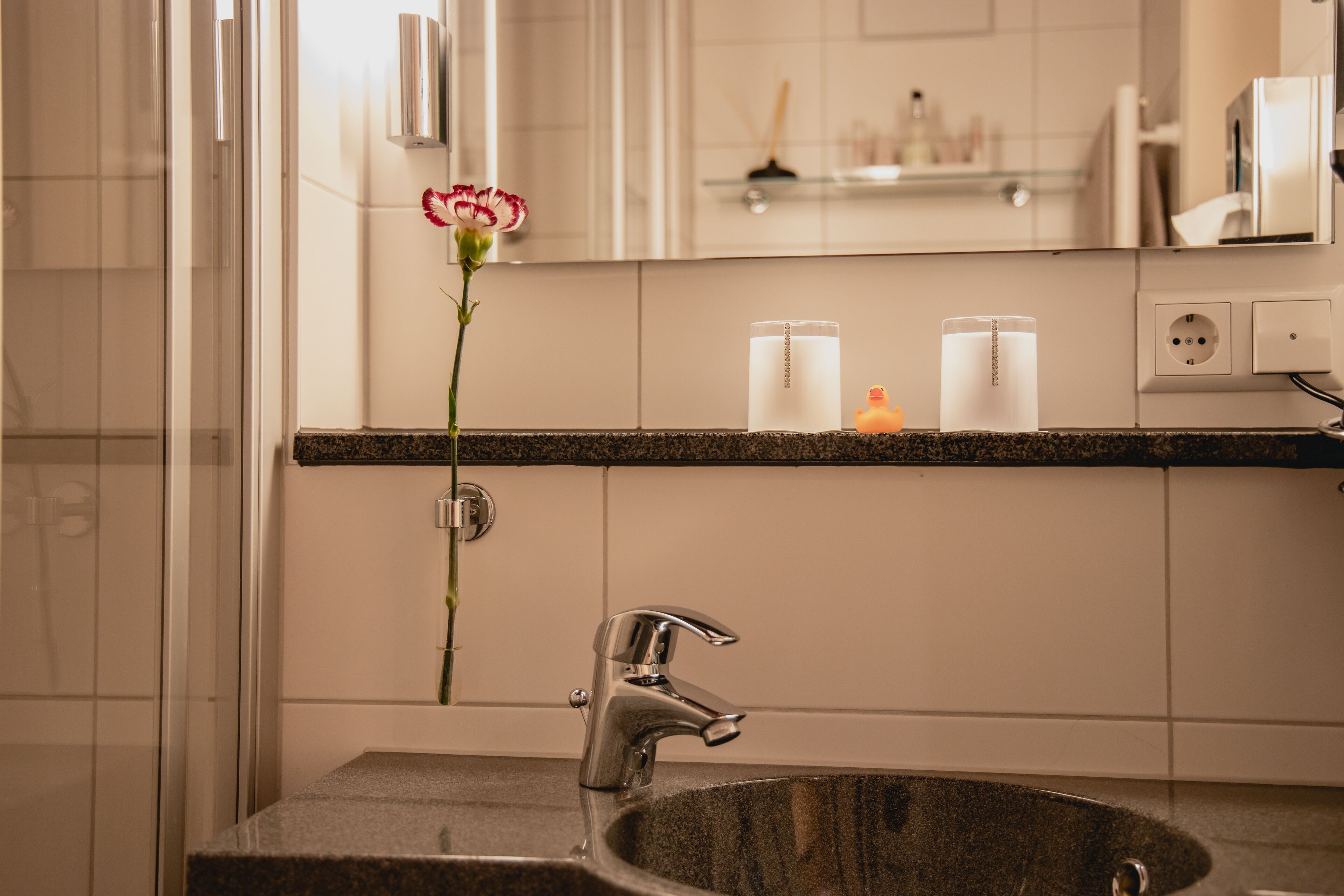 A bathroom with a granite sink, a mirror, and a vase with a single flower.