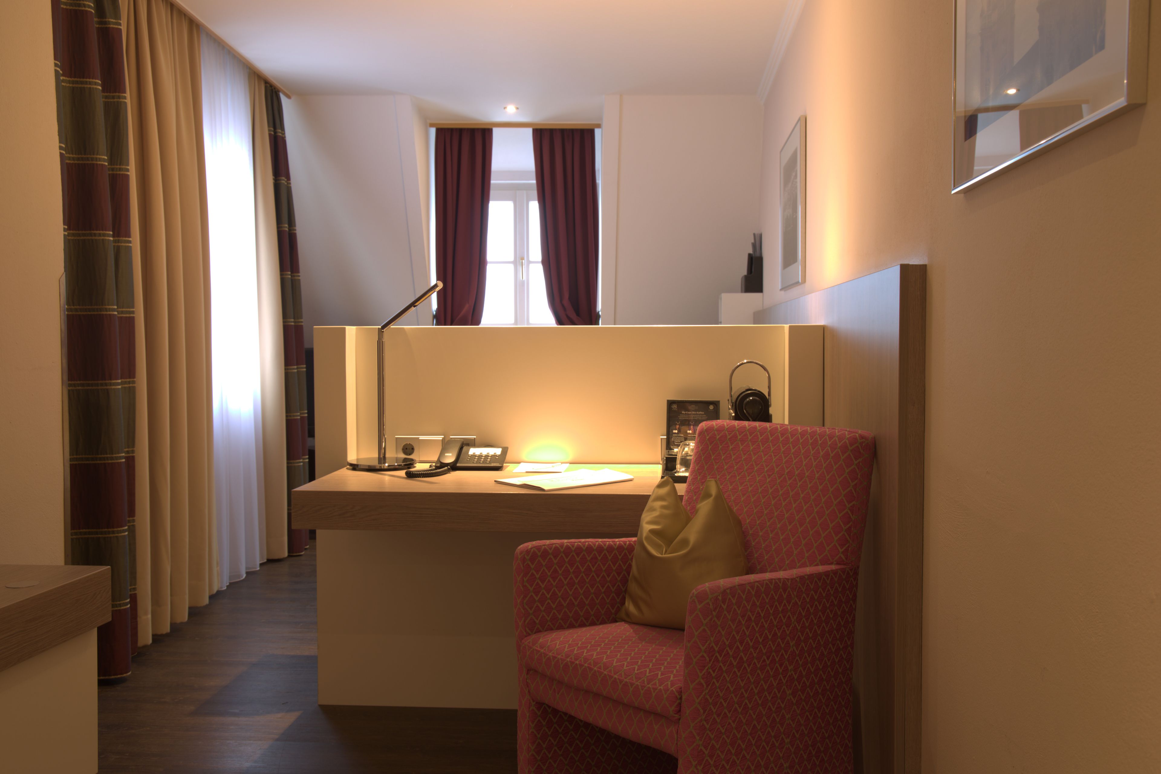 Ein Hotelzimmer mit Schreibtisch, Stuhl und einem Fenster mit Vorhängen.