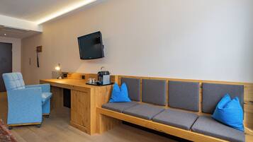A room with a wooden bench, a blue chair, a flat-screen TV mounted on the wall, and a coffee machine on the bench.