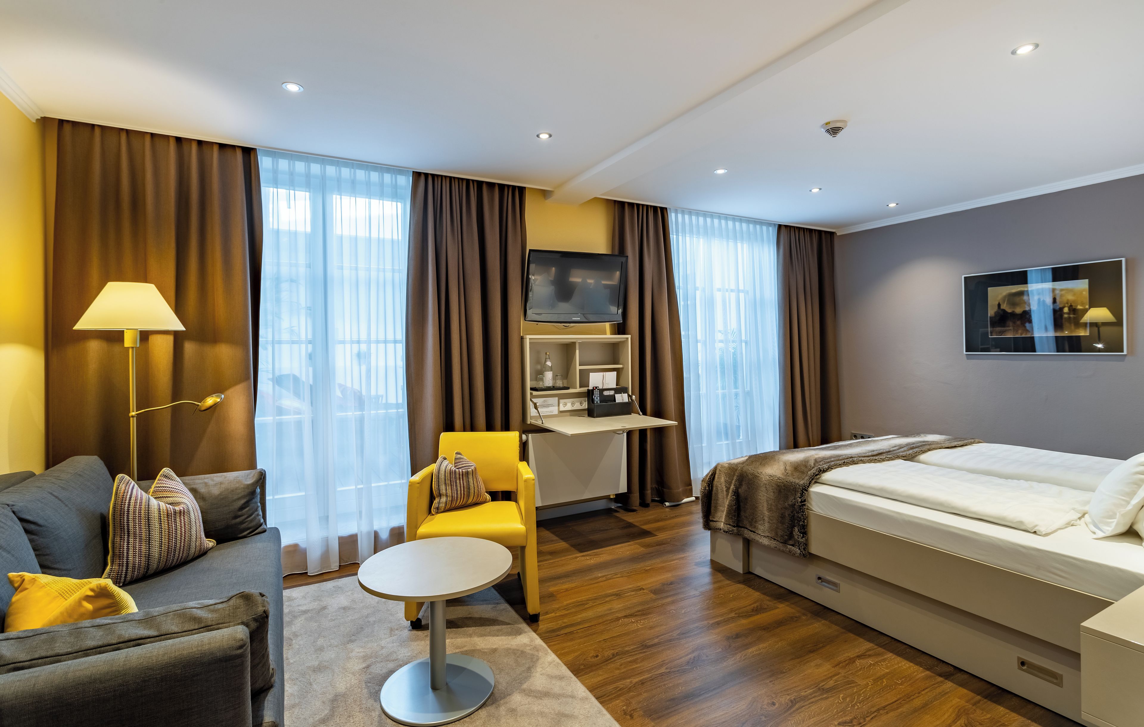 A hotel room with a bed, a desk, a chair, a sofa, and a TV.