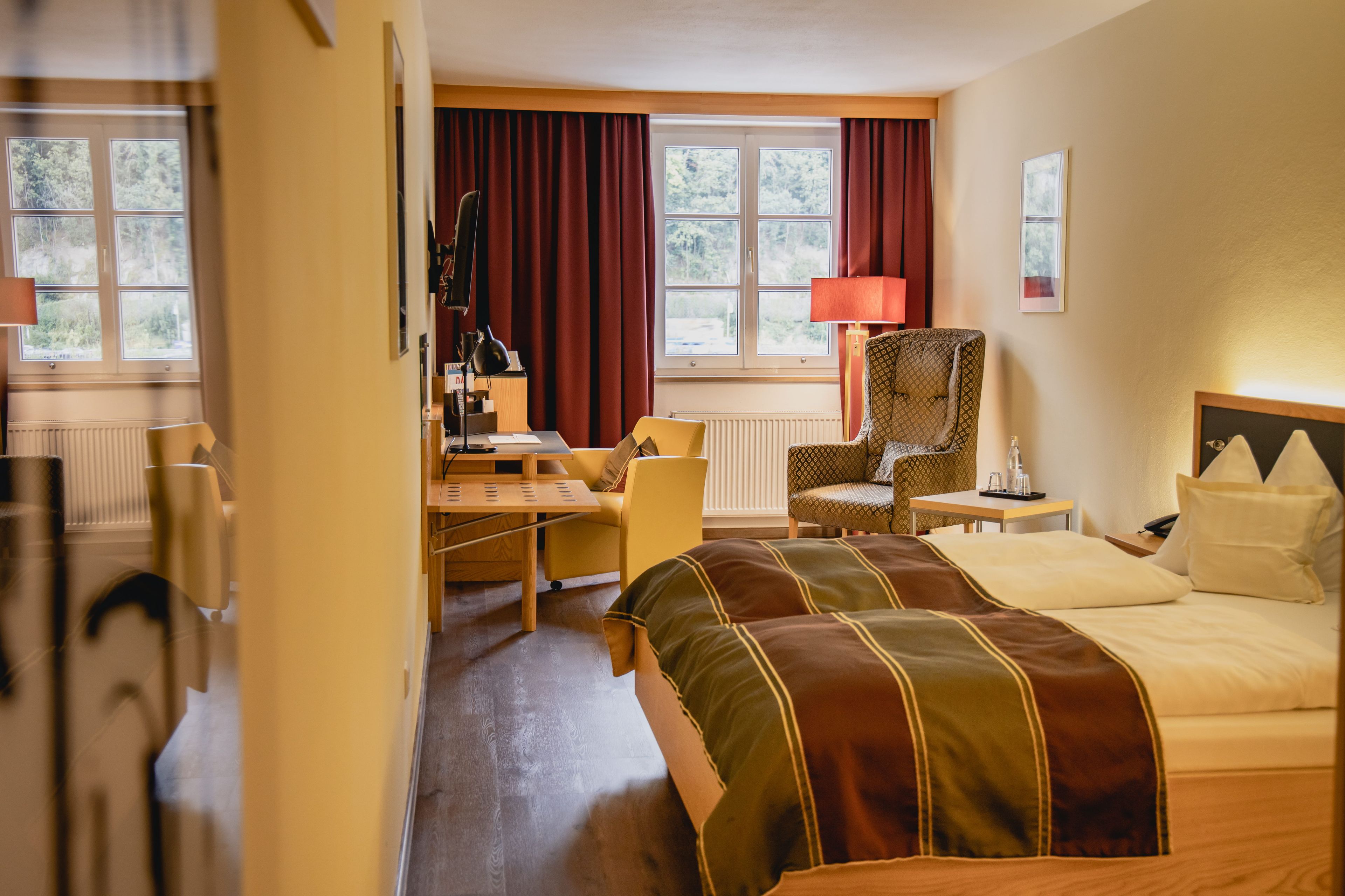 Ein Hotelzimmer mit zwei Betten, einem Schreibtisch, einem Stuhl und einem Fenster mit Vorhängen.