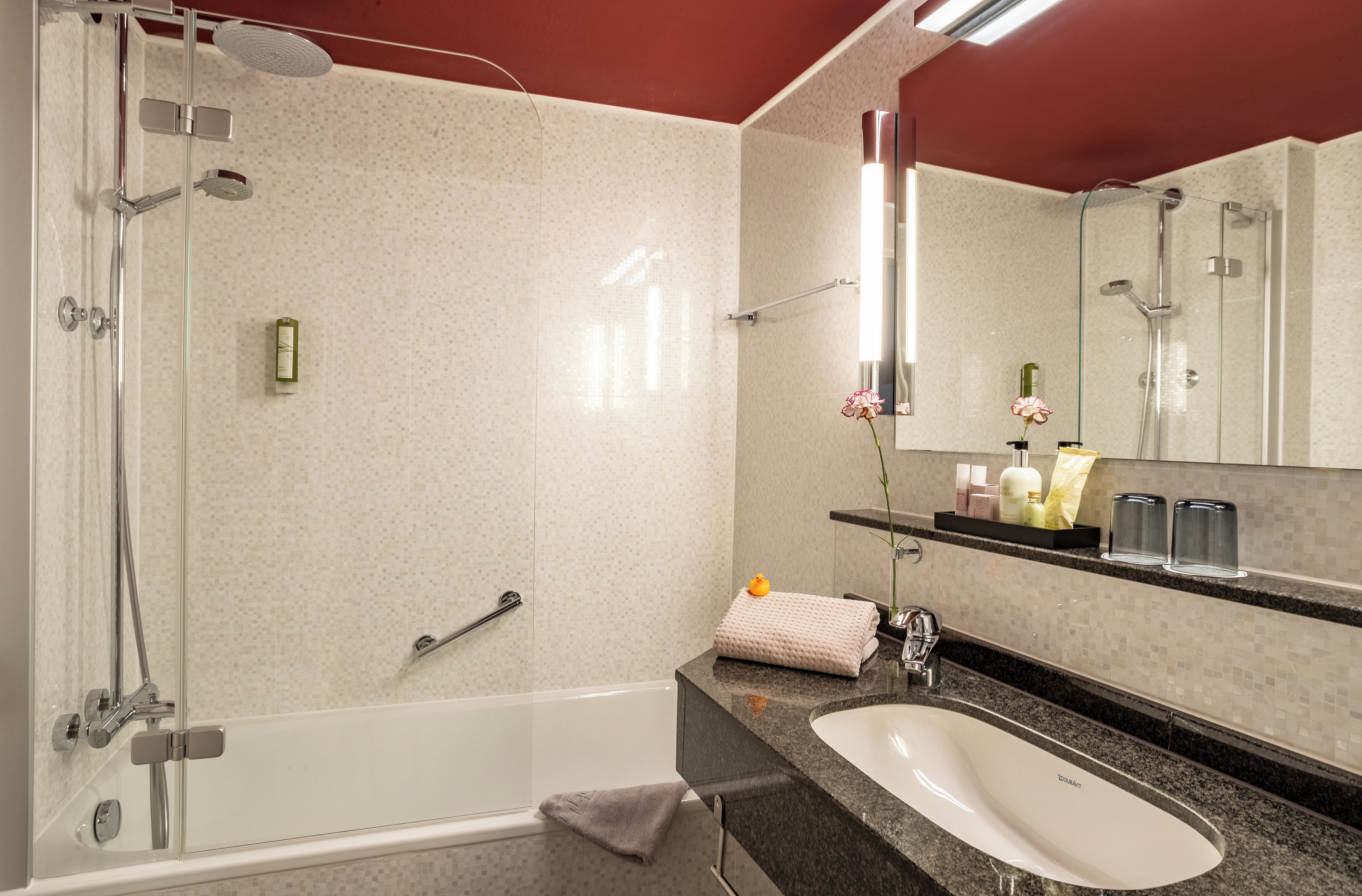 A modern bathroom with a glass-enclosed shower, a white bathtub, a granite countertop, and a mirror with a shelf above it.