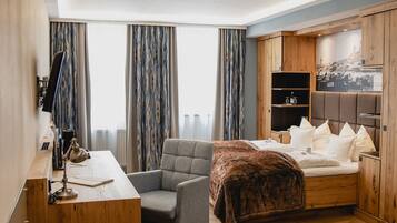 Habitación de hotel con un escritorio de madera, una silla cómoda, una cama con cabecera y un armario.