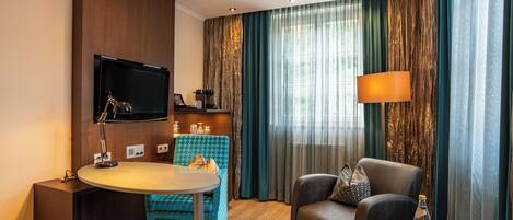Une chambre d’hôtel équipée d’un téléviseur à écran plat fixé au mur, d’une table ronde avec une chaise, d’un canapé et d’une petite table d’appoint sur laquelle se trouvent une bouteille et des verres.