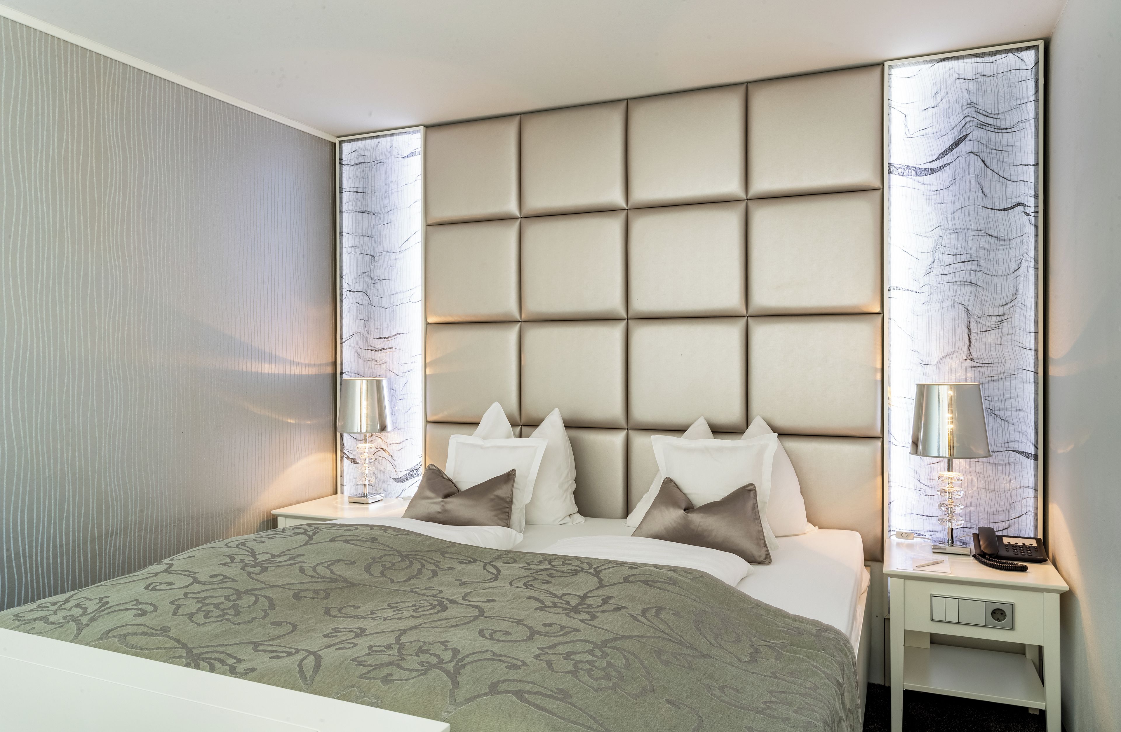 Ein Hotelzimmer mit einem großen Bett, einem gepolsterten Kopfteil, zwei Nachttischen mit Lampen und einer gemusterten Bettdecke.