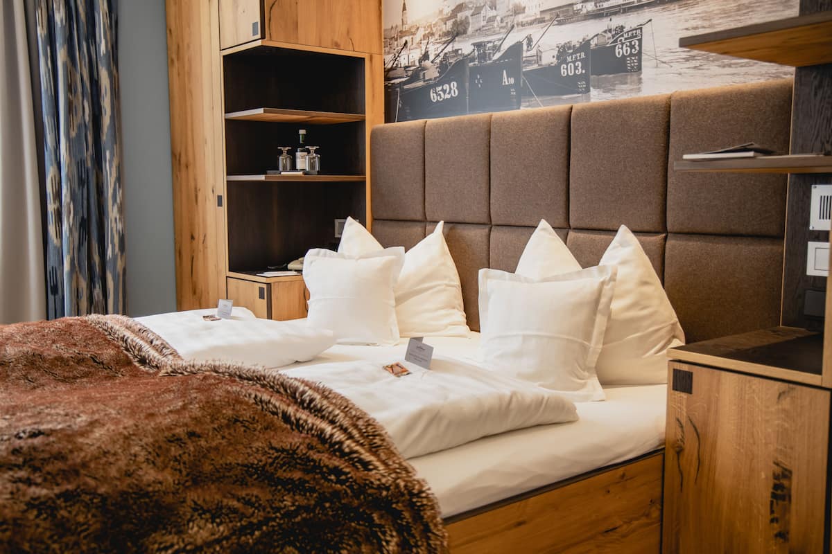 Ein Hotelzimmer mit einem Bett, einem hölzernen Kopfseitenverkleidung, einem Ablagefach mit Pflegeprodukten und einem Stadtplakat an der Wand.