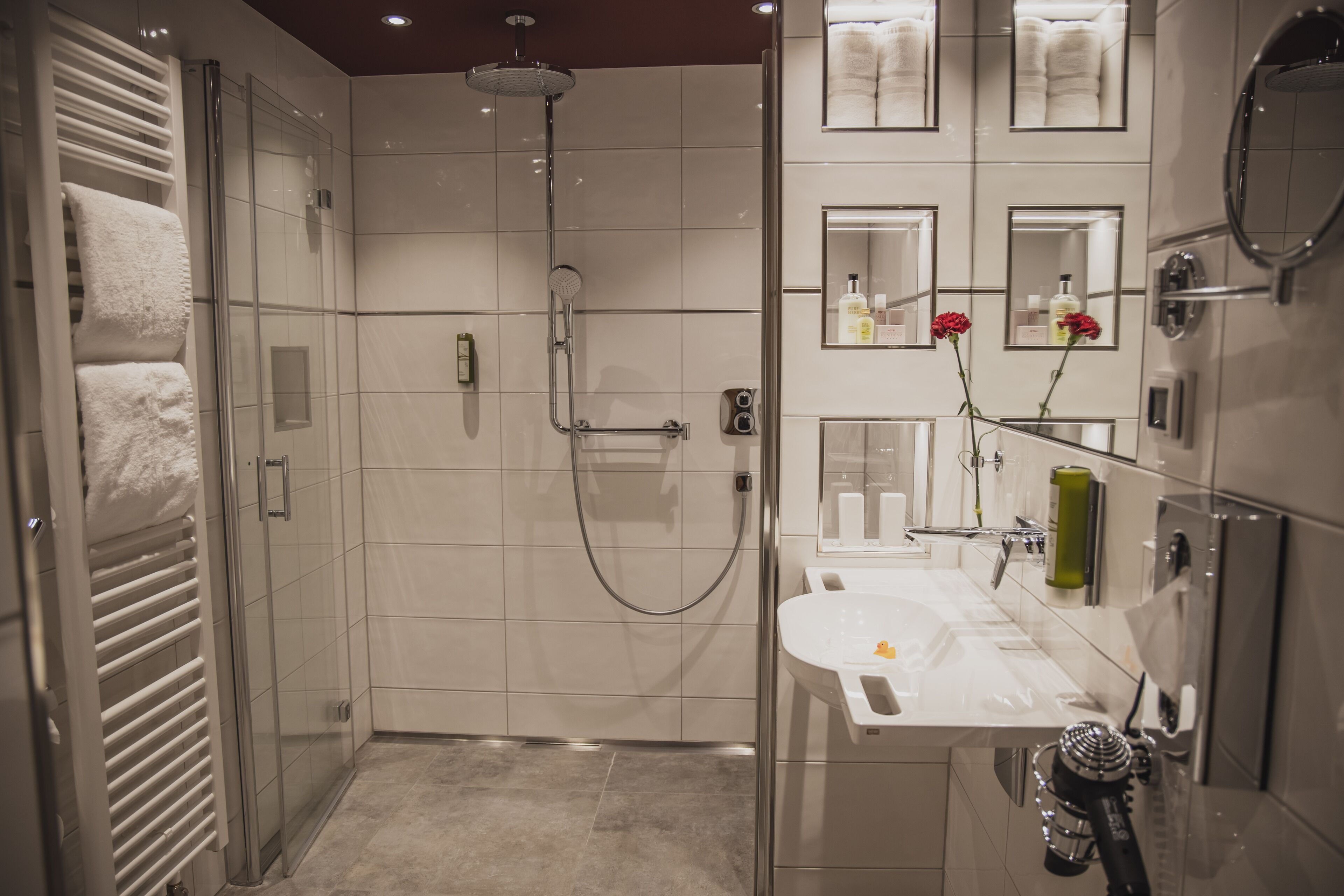 A modern bathroom with a glass-enclosed shower, a white sink, and a mirror with framed photos.