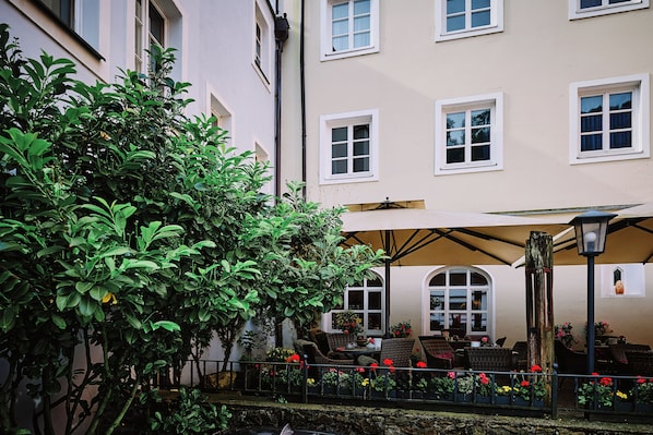 A courtyard with a covered seating area, a small garden, and a building with multiple windows. - Hotel Residenz Passau (Passau)