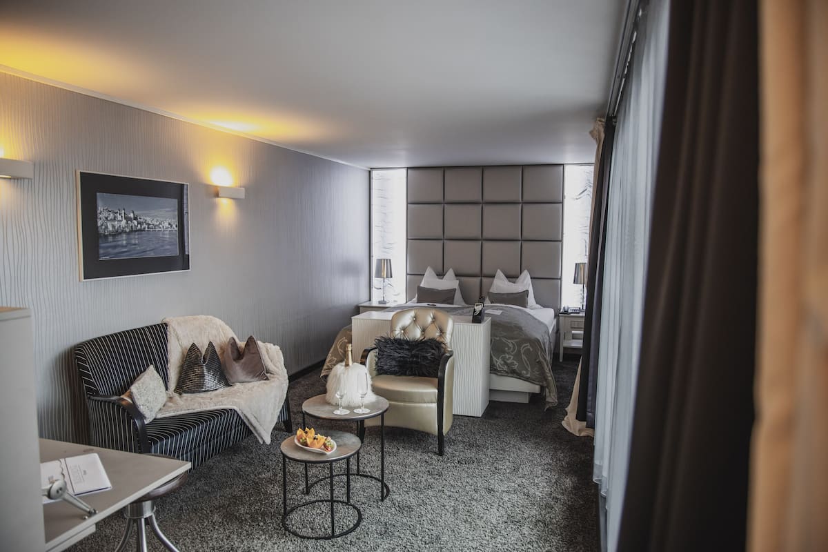 Ein Hotelzimmer mit Bett, einer Couch, einem kleinen Tisch mit Flasche und Gläsern sowie einem Sessel.