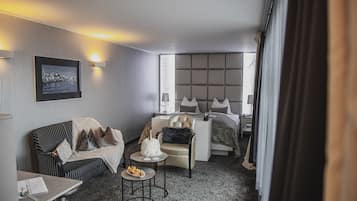 Hotelkamer met een bed, een bank, een kleine tafel met een fles en glazen, en een stoel.