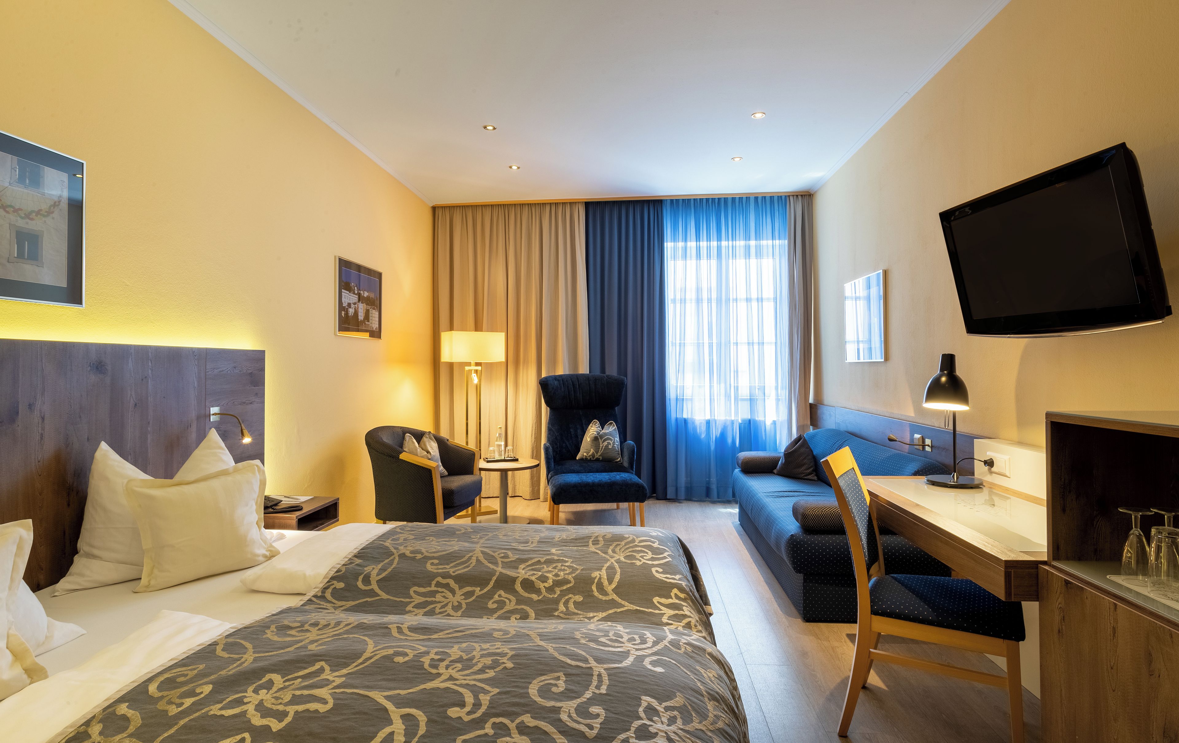 A hotel room with a bed, a desk, a chair, a TV, and a window with curtains.