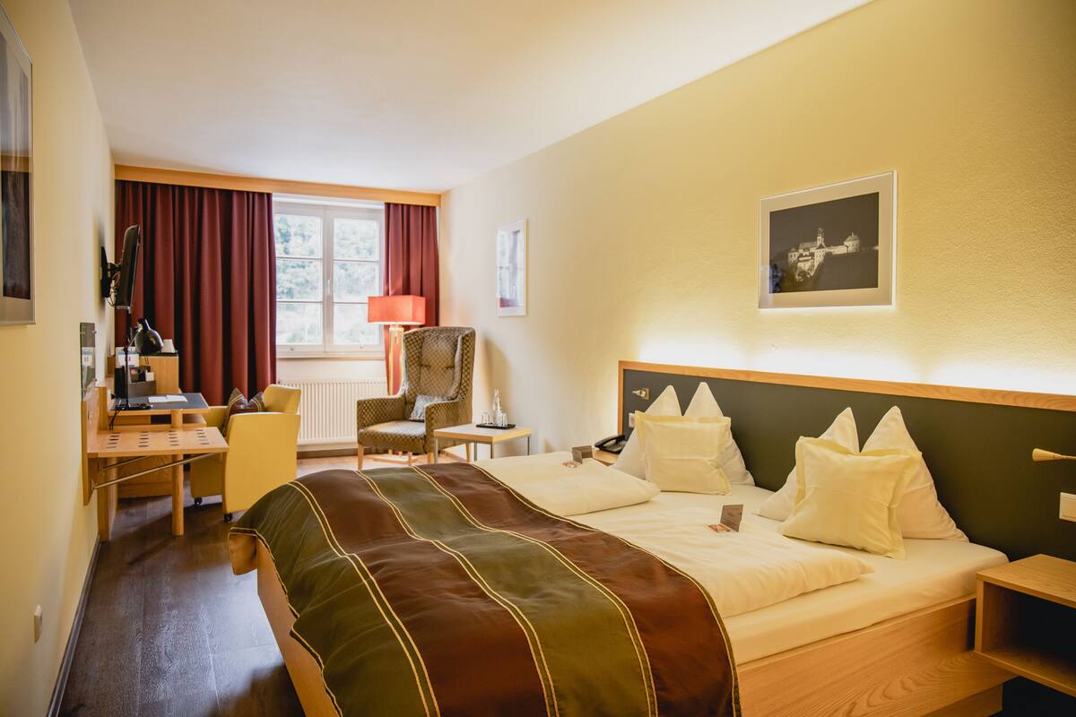 Ein Hotelzimmer mit Bett, Schreibtisch, Stuhl, Lampe und einem gerahmten Bild an der Wand.