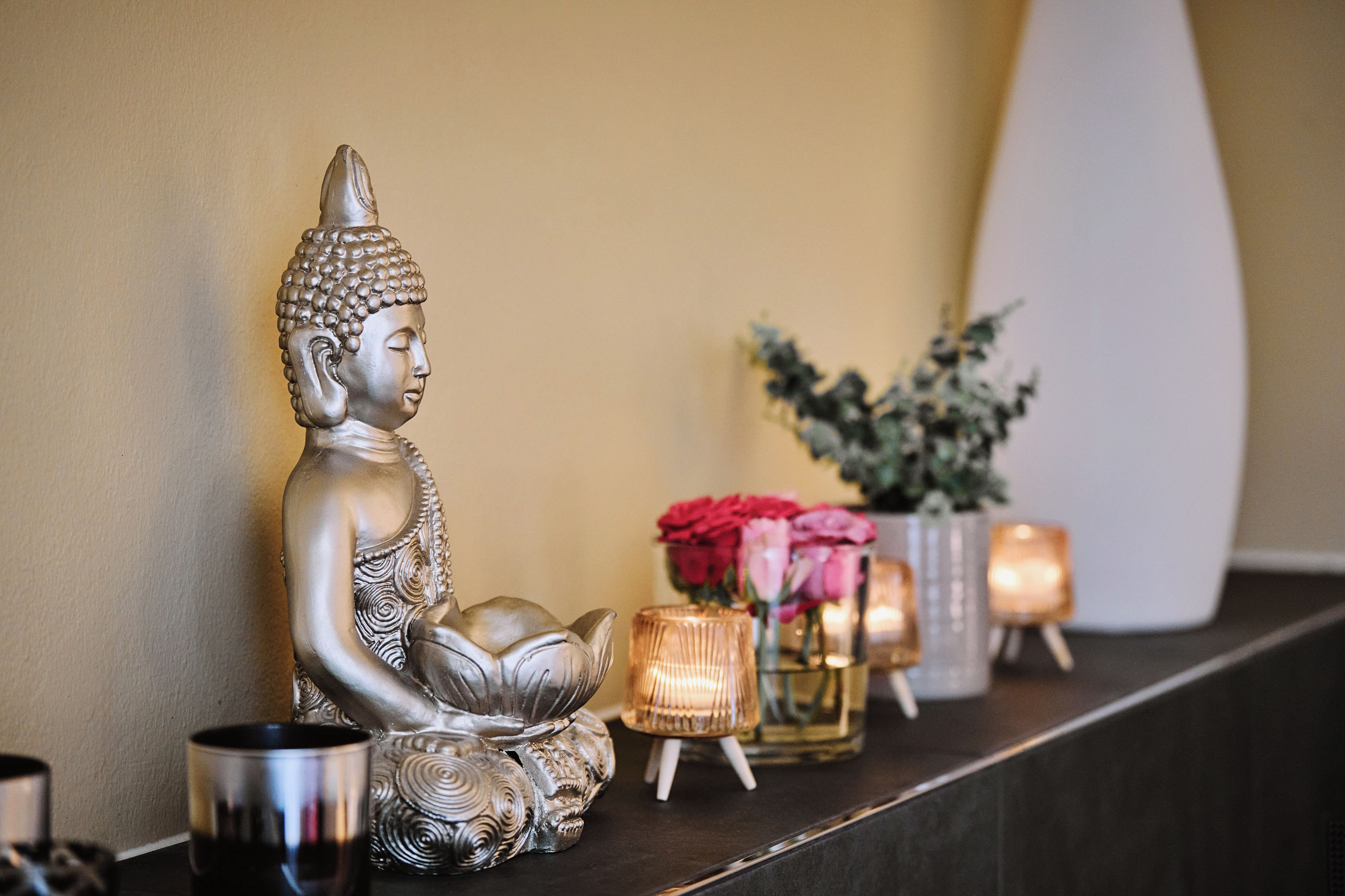 Une statue de Bouddha sur une étagère, entourée d’objets décoratifs et de bougies.