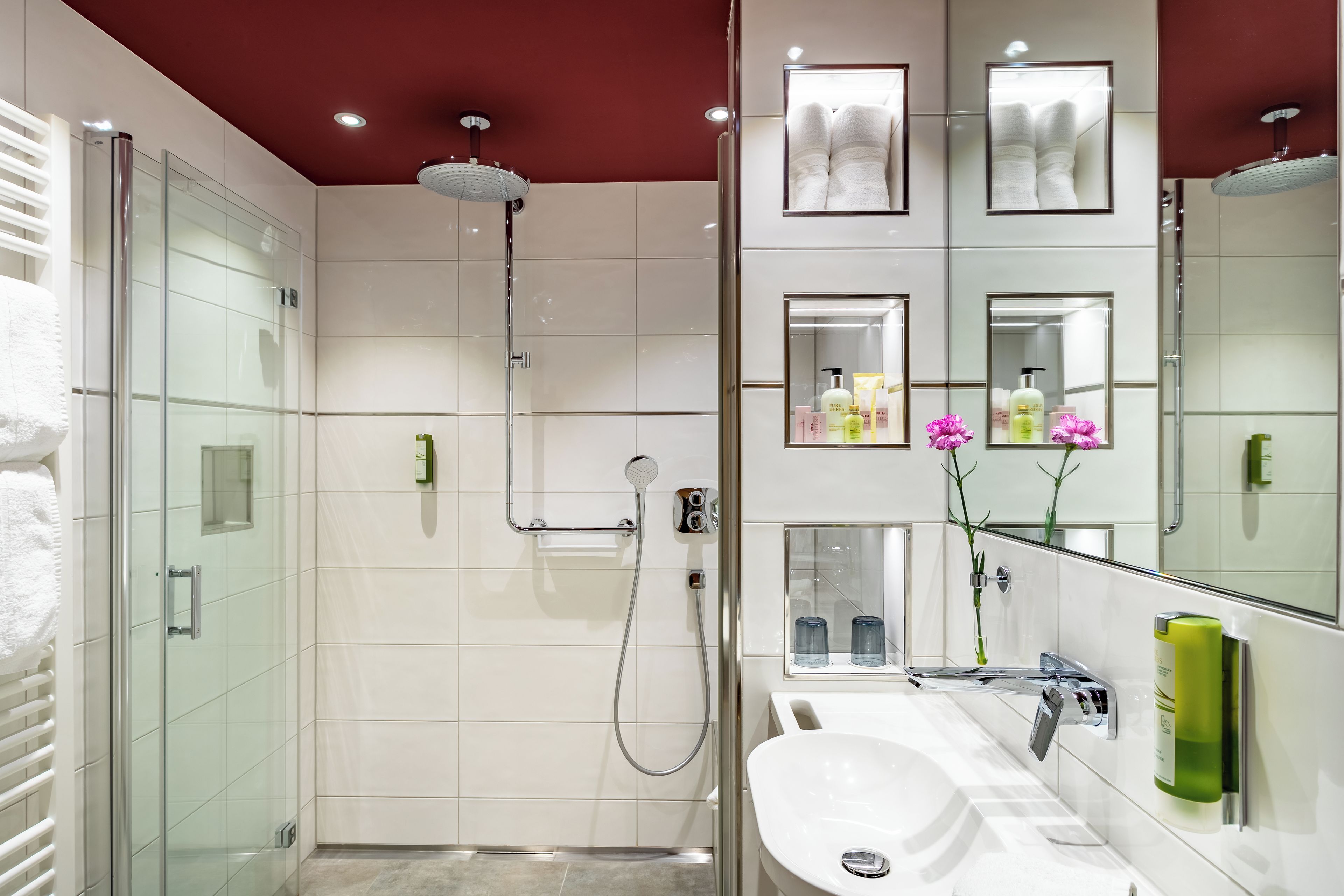 Un baño moderno con cabina de ducha de vidrio, lavabo blanco y tocador con espejos y artículos de aseo.