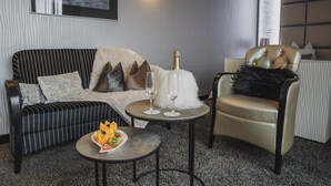 A modern living room with a striped sofa, a tufted armchair, a small round table with a bottle and glasses, and a fruit bowl. - Hotel Residenz Passau (Passau)