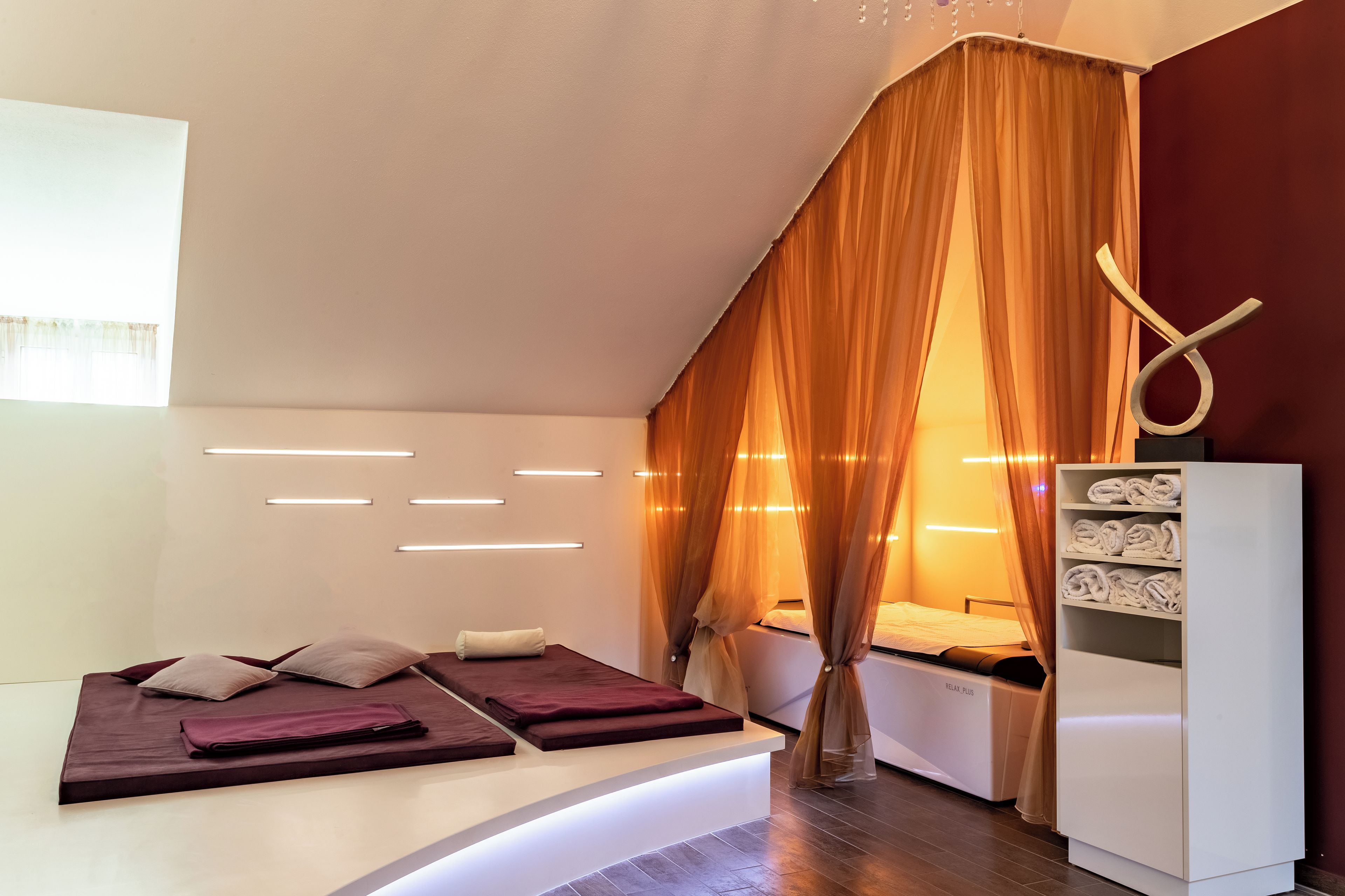 Habitación de hotel moderna con una cama, una camilla de masaje, un estante con toallas y una cortina.