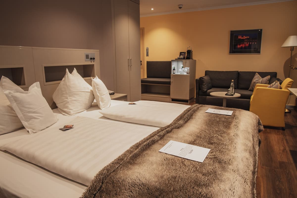 Ein Hotelzimmer mit zwei Betten, einem Sofa, einem kleinen Tisch und einem Kühlschrank.