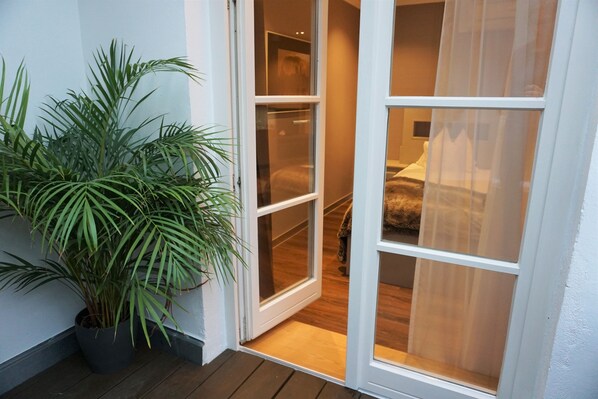 A room with a wooden floor, a bed with a white headboard, and a large potted plant by the door. - Hotel Residenz Passau (Passau)