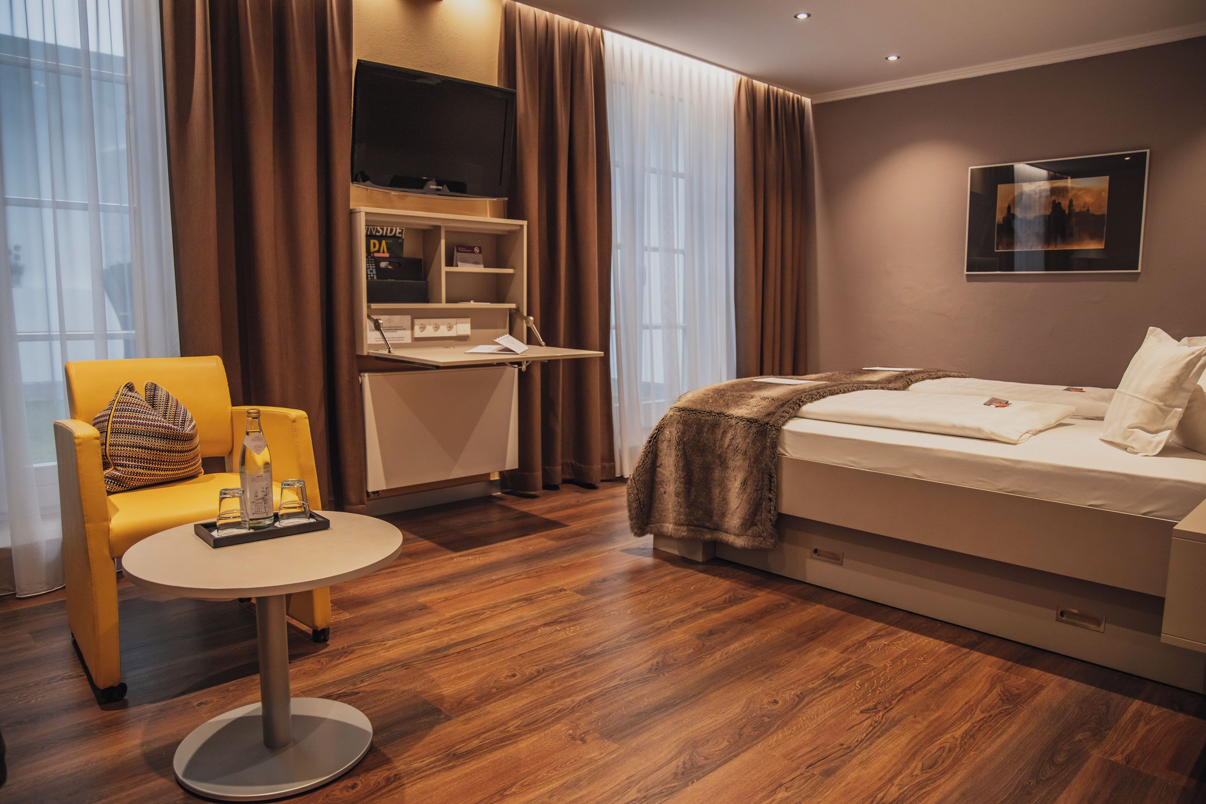 A hotel room with a bed, a desk, a chair, and a television.