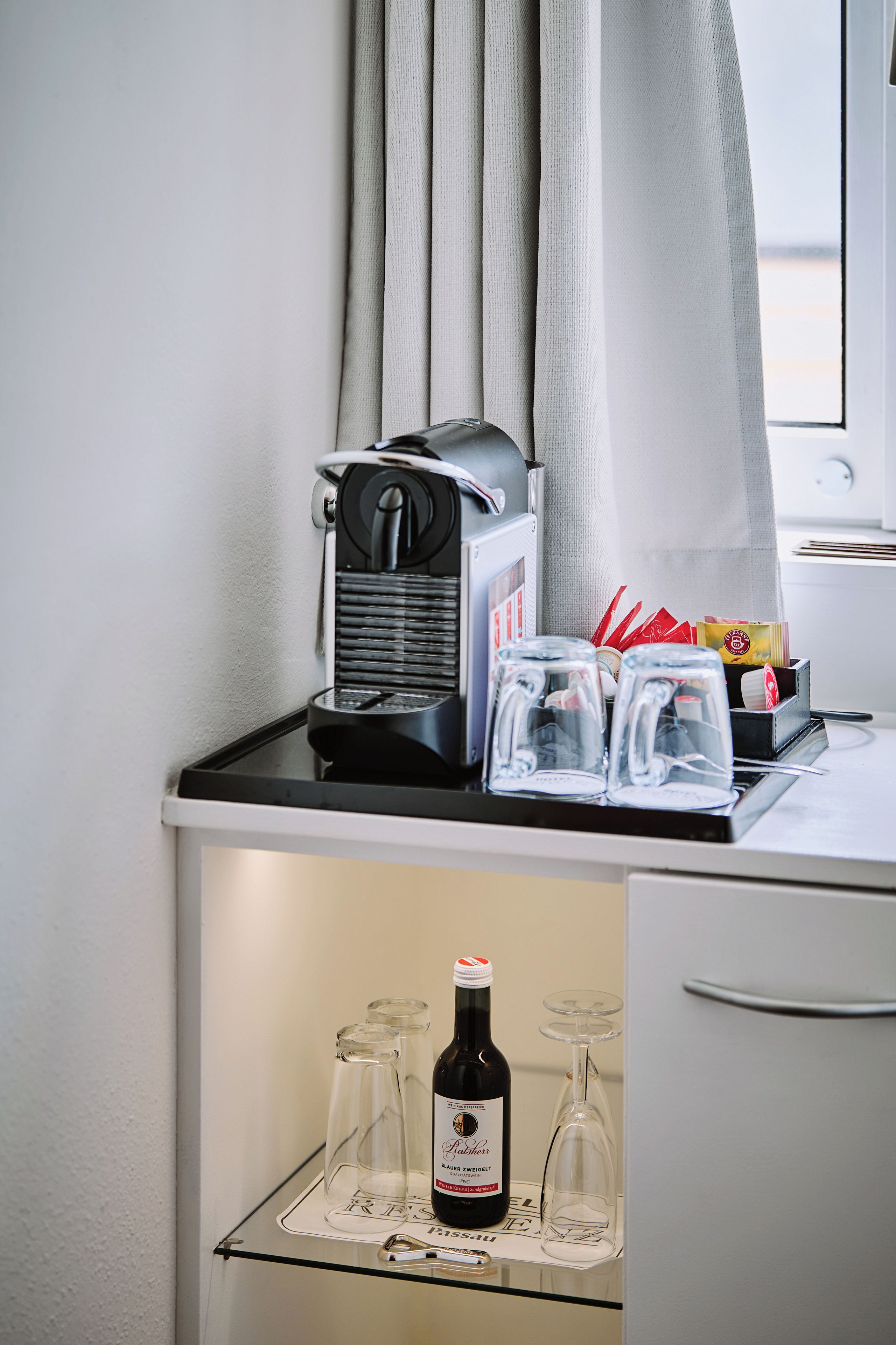 A kitchenette with a coffee machine, a wine bottle, and glasses on a counter.
