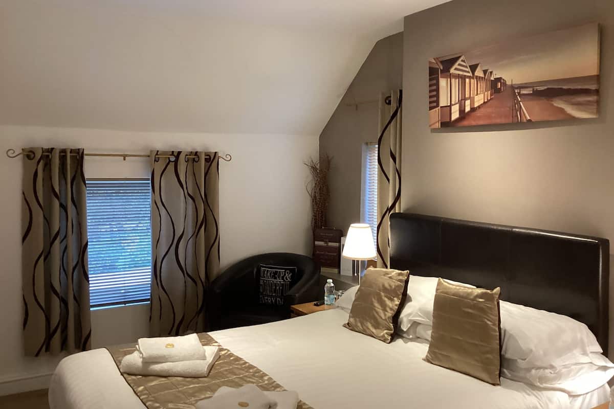 A hotel room with a bed, a desk, a chair, a lamp, and a painting on the wall.
