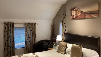 Habitación de hotel con cama, escritorio, silla, lámpara y un cuadro en la pared.