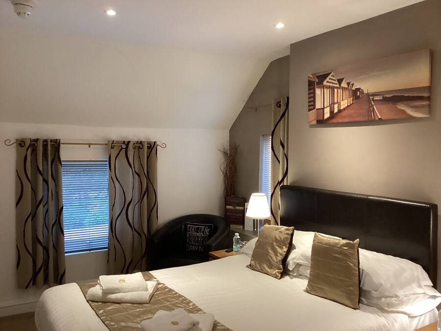 Habitación de hotel con cama, escritorio, silla, lámpara y un cuadro en la pared.