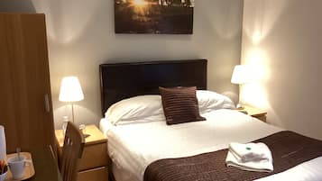 Een hotelkamer met een bed, twee bedlampen, een nachtkastje, een houten garderobe en een schilderij aan de muur.