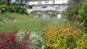 A two-story house with a well-maintained lawn and garden in the foreground. - The Manian (Kilgetty)