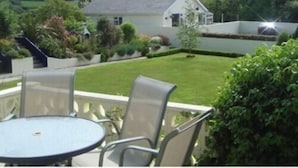 A patio with a round table and chairs, a white house in the background, and a well-maintained lawn. - The Manian (Kilgetty)